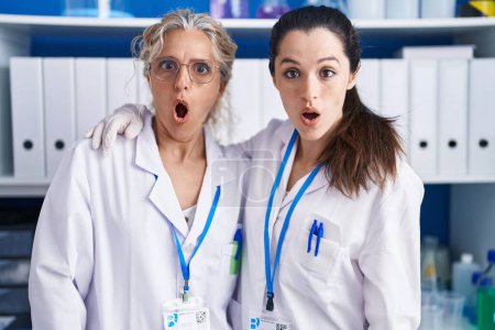 Téléchargez les photos : Mère et fille travaillant au laboratoire scientifique effrayés et étonnés avec la bouche ouverte pour surprise, visage d'incrédulité - en image libre de droit