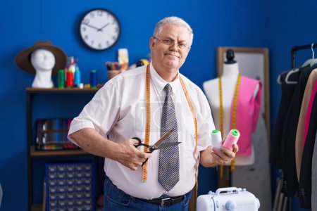 Téléchargez les photos : Middle age grey-haired man tailor smiling confident holding scissors and thread at tailor shop - en image libre de droit
