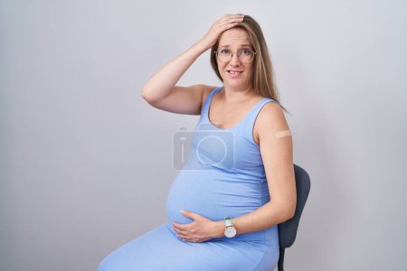 Photo for Young pregnant woman wearing band aid for vaccine injection stressed and frustrated with hand on head, surprised and angry face - Royalty Free Image