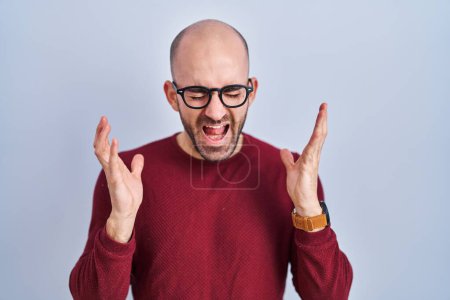 Photo for Young bald man with beard standing over white background wearing glasses celebrating mad and crazy for success with arms raised and closed eyes screaming excited. winner concept - Royalty Free Image