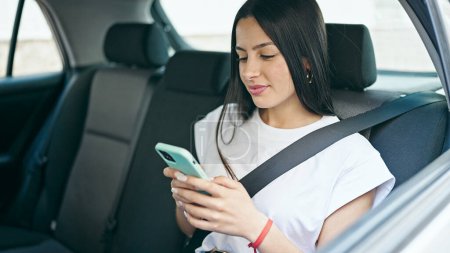 Foto de Joven hermosa mujer hispana pasajero usando teléfono inteligente sentado en el coche en la calle - Imagen libre de derechos