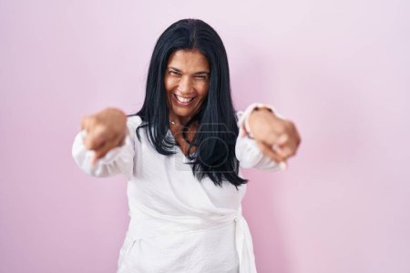 Photo for Mature hispanic woman standing over pink background pointing to you and the camera with fingers, smiling positive and cheerful - Royalty Free Image