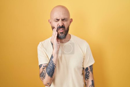 Téléchargez les photos : Hispanic man with tattoos standing over yellow background touching mouth with hand with painful expression because of toothache or dental illness on teeth. dentist - en image libre de droit