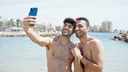Foto de Dos hombres turista pareja sonriendo confiado hacer selfie por teléfono inteligente en la playa - Imagen libre de derechos
