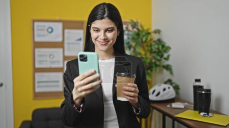 Photo for Young beautiful hispanic woman business worker using smartphone drinking coffee at office - Royalty Free Image