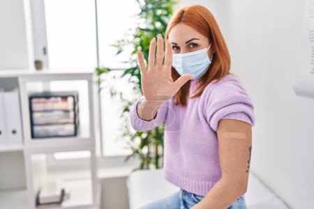 Photo for Young woman getting vaccine showing arm with band aid with open hand doing stop sign with serious and confident expression, defense gesture - Royalty Free Image