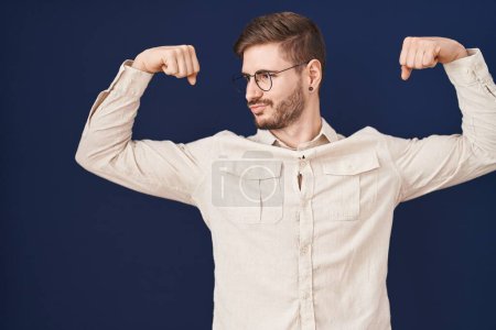 Photo for Hispanic man with beard standing over blue background showing arms muscles smiling proud. fitness concept. - Royalty Free Image