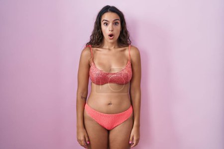 Foto de Mujer hispana joven vistiendo lencería sobre fondo rosa asustada y conmocionada con expresión sorpresa y asombrada, miedo y cara excitada. - Imagen libre de derechos