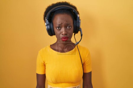 Foto de Mujer africana con el pelo rizado de pie sobre el fondo amarillo con auriculares deprimidos y preocupación por la angustia, llorando enojado y asustado. expresión triste. - Imagen libre de derechos