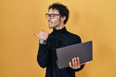 Foto de Hombre hispano trabajando usando computadora portátil apuntando el pulgar hacia el lado sonriendo feliz con la boca abierta - Imagen libre de derechos
