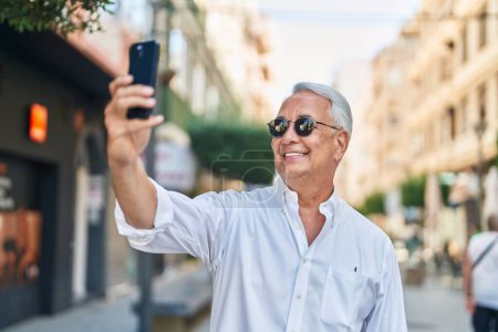 Photo for Middle age grey-haired man smiling confident making selfie by the smartphone at street - Royalty Free Image