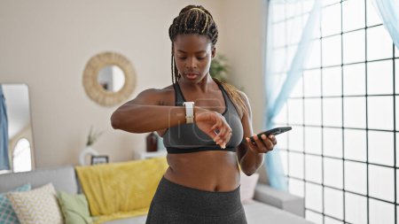 Photo for African american woman wearing sportswear using smartphone and watch at home - Royalty Free Image
