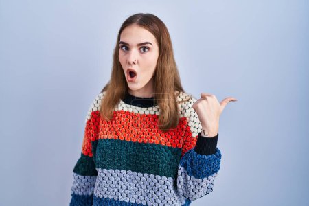 Photo for Young hispanic girl standing over blue background surprised pointing with hand finger to the side, open mouth amazed expression. - Royalty Free Image