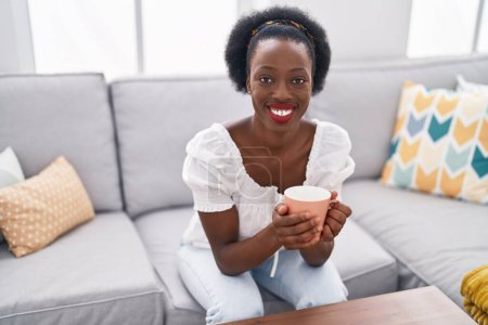 Photo for African american woman drinking coffee sitting on sofa at home - Royalty Free Image