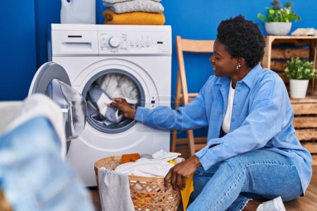 Foto de Mujer afroamericana sonriendo confiada usando lavadora en la sala de lavandería - Imagen libre de derechos