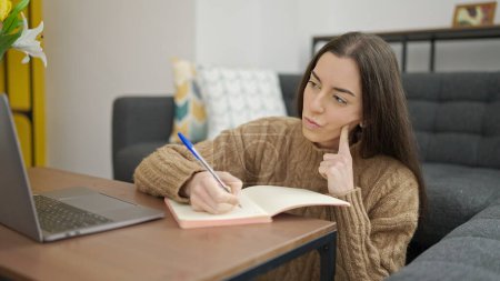 Foto de Mujer hispana hermosa joven usando la escritura del ordenador portátil en el cuaderno en casa - Imagen libre de derechos