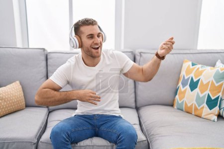 Photo for Young caucasian man listening to music doing guitar gesture at home - Royalty Free Image