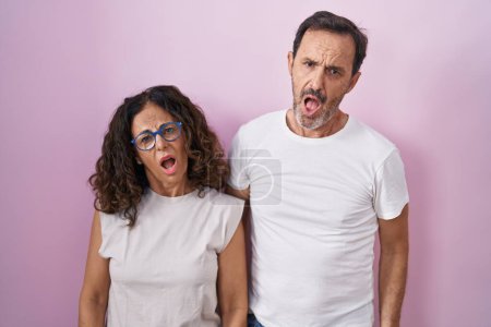 Photo for Middle age hispanic couple together over pink background in shock face, looking skeptical and sarcastic, surprised with open mouth - Royalty Free Image