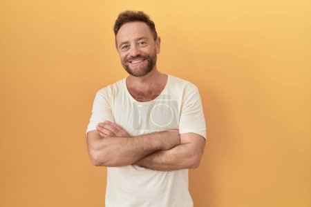 Téléchargez les photos : Middle age man with beard standing over yellow background happy face smiling with crossed arms looking at the camera. positive person. - en image libre de droit
