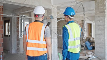 Téléchargez les photos : Deux constructeurs hommes debout ensemble vers l'arrière sur le chantier de construction - en image libre de droit