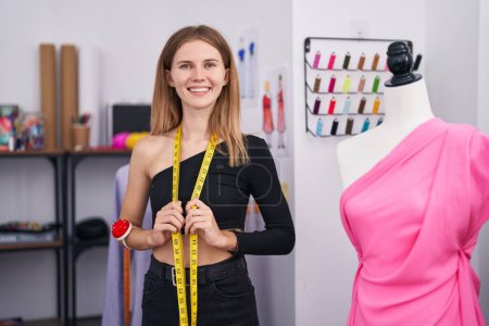 Téléchargez les photos : Jeune femme blonde tailleur souriant avec confiance ruban à mesurer au magasin de tailleur - en image libre de droit