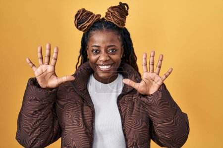 Téléchargez les photos : Femme africaine avec les cheveux tressés debout sur fond jaune montrant et pointant vers le haut avec les doigts numéro dix tout en souriant confiant et heureux. - en image libre de droit