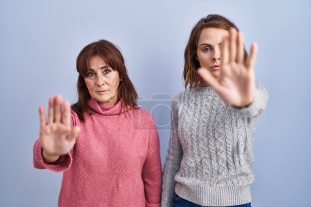 Photo for Mother and daughter standing over blue background doing stop sing with palm of the hand. warning expression with negative and serious gesture on the face. - Royalty Free Image