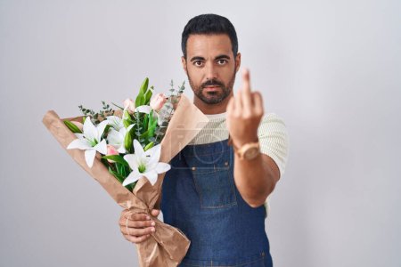 Téléchargez les photos : Hispanic man with beard working as florist showing middle finger, impolite and rude fuck off expression - en image libre de droit