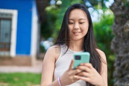 Photo for Young chinese woman smiling confident using smartphone at park - Royalty Free Image