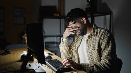 Foto de Joven trabajador de negocios hispano usando computadora estresada en oficina - Imagen libre de derechos