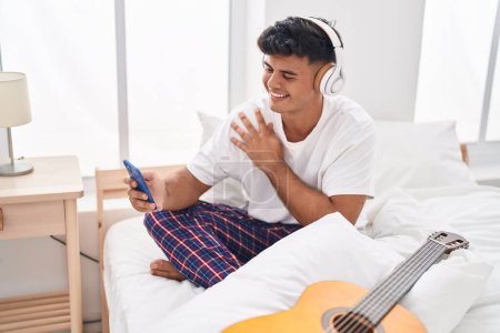 Photo for Young hispanic man listening to music sitting on bed at bedroom - Royalty Free Image