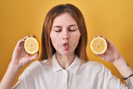 Téléchargez les photos : Belle femme tenant des citrons faisant visage de poisson avec la bouche et les yeux plissés, fou et comique. - en image libre de droit