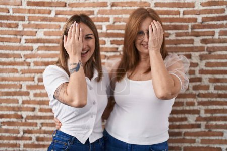 Foto de Hispanic mother and daughter wearing casual white t shirt covering one eye with hand, confident smile on face and surprise emotion. - Imagen libre de derechos