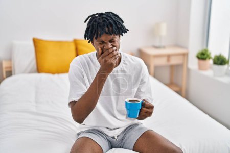 Téléchargez les photos : African american man tired drinking cup of coffee sitting on bed at bedroom - en image libre de droit