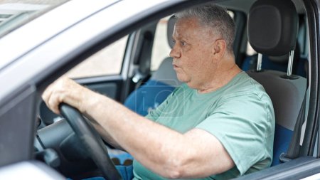 Téléchargez les photos : Homme aux cheveux gris d'âge moyen conduisant une voiture dans la rue - en image libre de droit