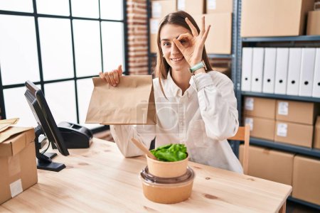 Photo for Young caucasian woman working at small business ecommerce holding take away food smiling happy doing ok sign with hand on eye looking through fingers - Royalty Free Image