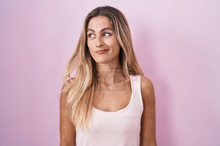Photo for Young blonde woman standing over pink background smiling looking to the side and staring away thinking. - Royalty Free Image