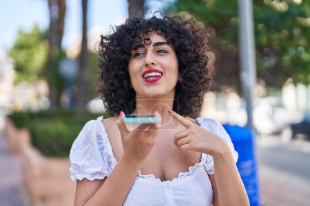 Téléchargez les photos : Jeune femme du Moyen-Orient souriant confiant parler sur le smartphone au parc - en image libre de droit