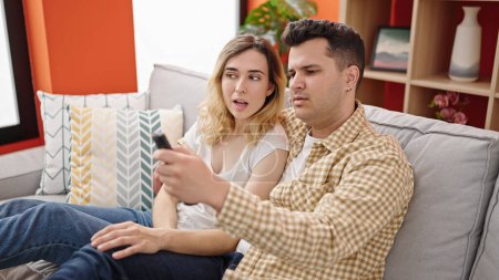 Téléchargez les photos : Homme et femme couple assis sur le canapé regarder la télévision à la maison - en image libre de droit