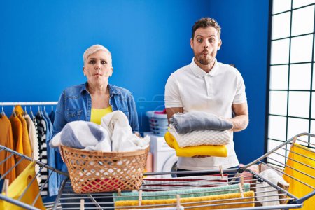 Photo for Hispanic mother and son hanging clothes at clothesline making fish face with mouth and squinting eyes, crazy and comical. - Royalty Free Image