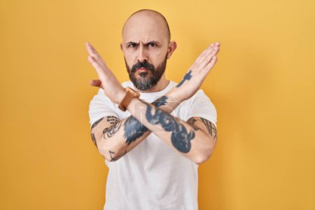 Téléchargez les photos : Jeune homme hispanique avec des tatouages debout sur fond jaune expression de rejet croisant les bras faisant signe négatif, visage en colère - en image libre de droit