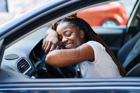 Téléchargez les photos : Femme afro-américaine souriante confiante penchée sur le volant dans la rue - en image libre de droit