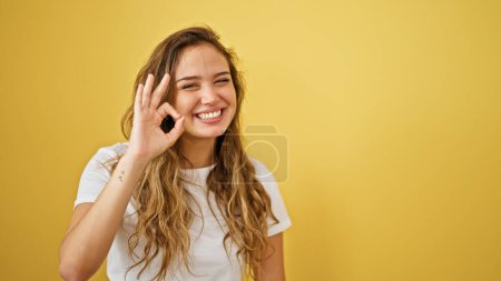 Foto de Joven hermosa mujer hispana sonriendo confiada haciendo buen gesto sobre aislado fondo amarillo - Imagen libre de derechos