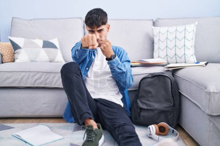 Photo for Young hispanic man sitting on the floor studying for university punching fist to fight, aggressive and angry attack, threat and violence - Royalty Free Image