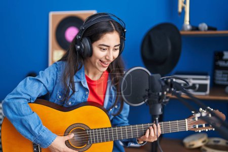Foto de Joven chica hispana músico cantando canción tocando guitarra clásica en el estudio de música - Imagen libre de derechos