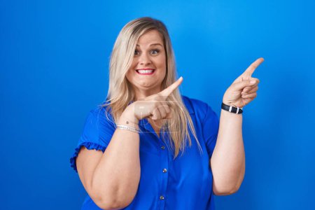 Photo for Caucasian plus size woman standing over blue background smiling and looking at the camera pointing with two hands and fingers to the side. - Royalty Free Image
