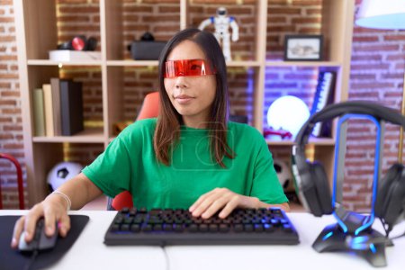 Photo for Middle age chinese woman wearing virtual reality glasses looking away to side with smile on face, natural expression. laughing confident. - Royalty Free Image