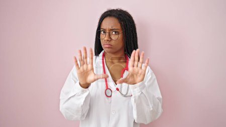 Foto de Médico afroamericano haciendo gesto de espera sobre fondo rosa aislado - Imagen libre de derechos