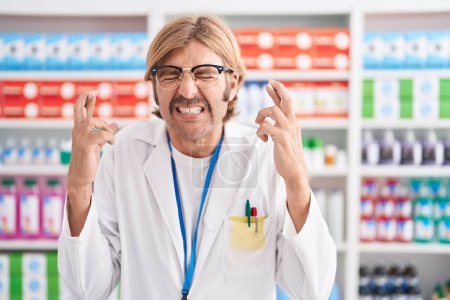 Téléchargez les photos : Homme caucasien avec moustache travaillant à la pharmacie pharmacie geste doigt croisé souriant avec espoir et les yeux fermés. chance et concept superstitieux. - en image libre de droit