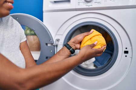 Téléchargez les photos : Femme afro-américaine mettre des vêtements sur la machine à laver à la buanderie - en image libre de droit